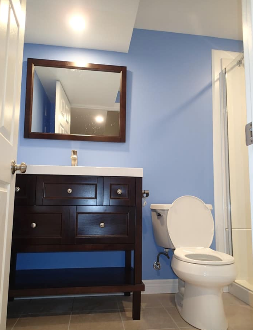 A small bathroom with blue walls, a dark wood vanity, and an open-lid toilet.
