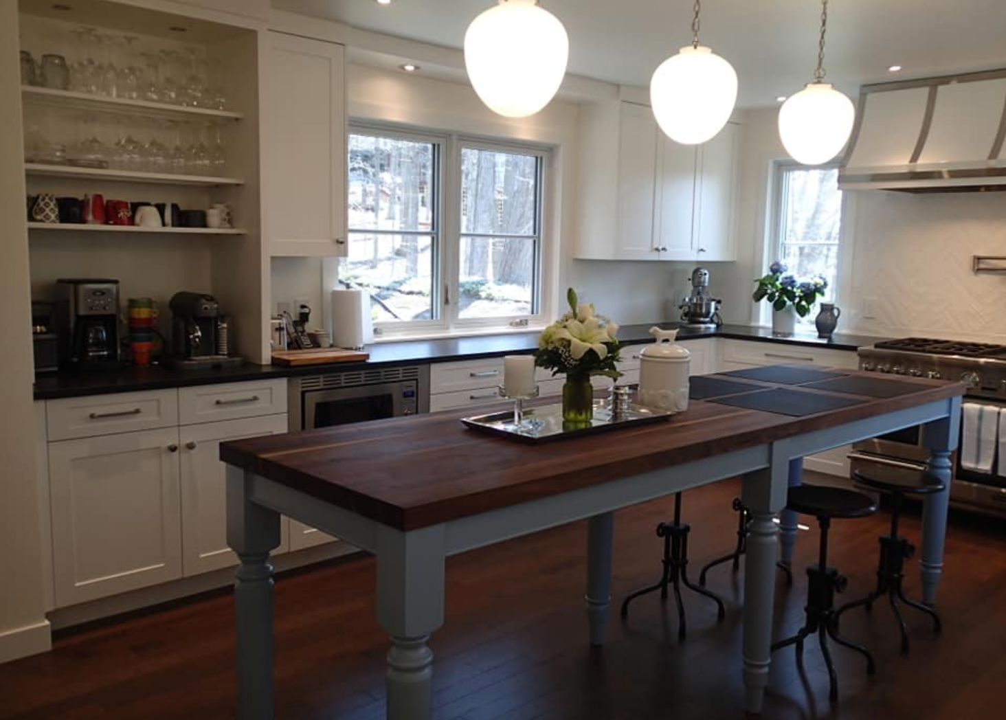 Bright kitchen with white cabinets, a dark wood island, and three pendant lights.