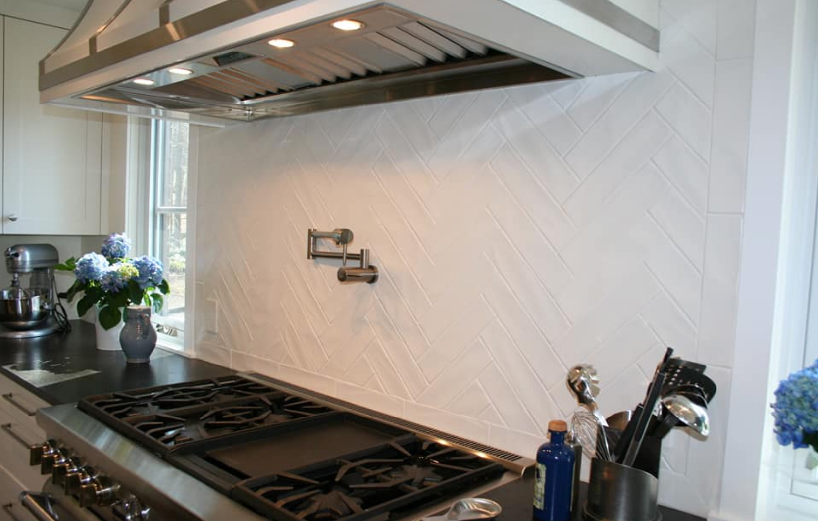 Kitchen with white tile backsplash, stainless range hood, and gas stovetop.