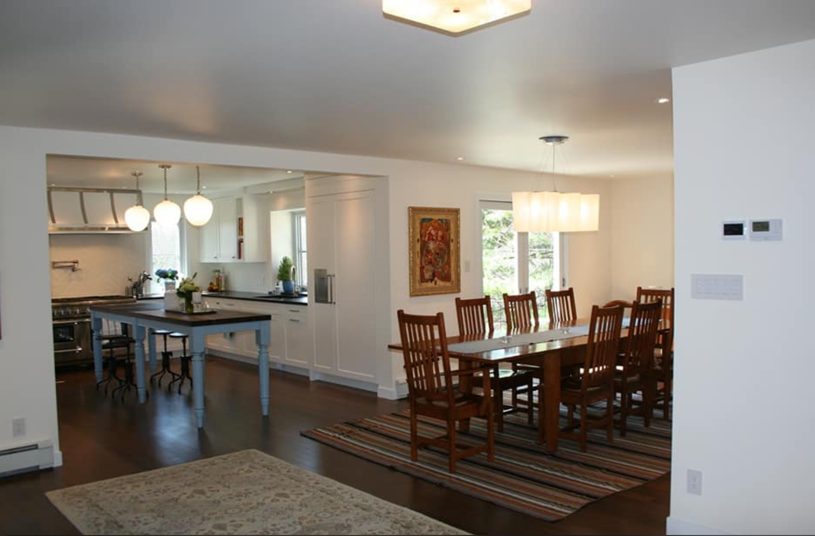 Open-concept kitchen and dining area with dark wood floors, white walls, and a long dining table.