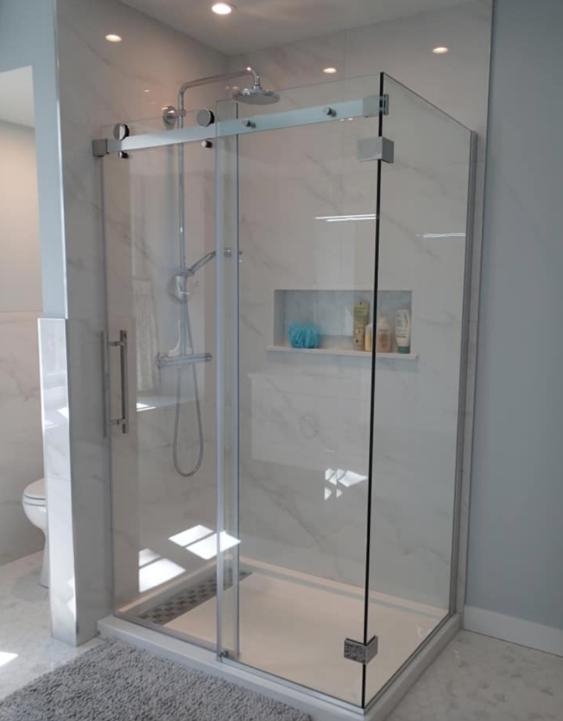 Modern glass shower with a sliding door and built-in shelf, tiled with white marble and recessed lighting.