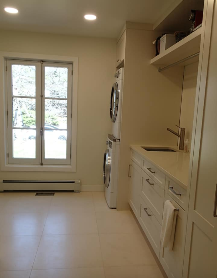 Laundry room with white cabinets, stacked washer/dryer, window, and sink.