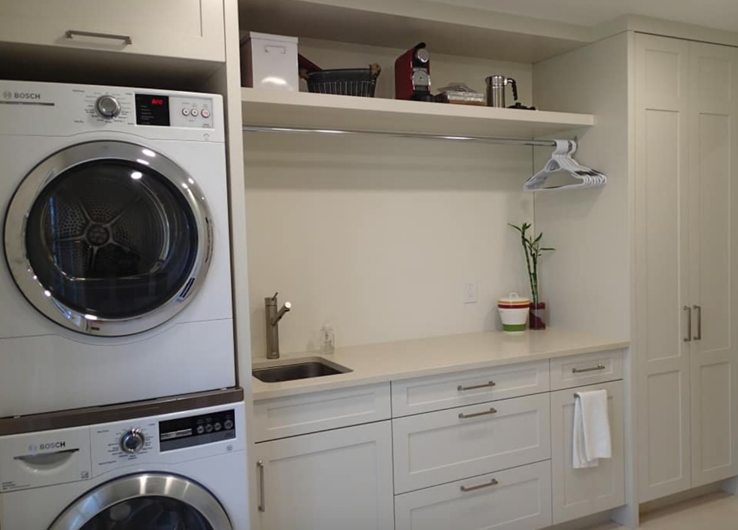 A laundry room with a stacked washer/dryer, sink, cabinets, and a floating shelf.