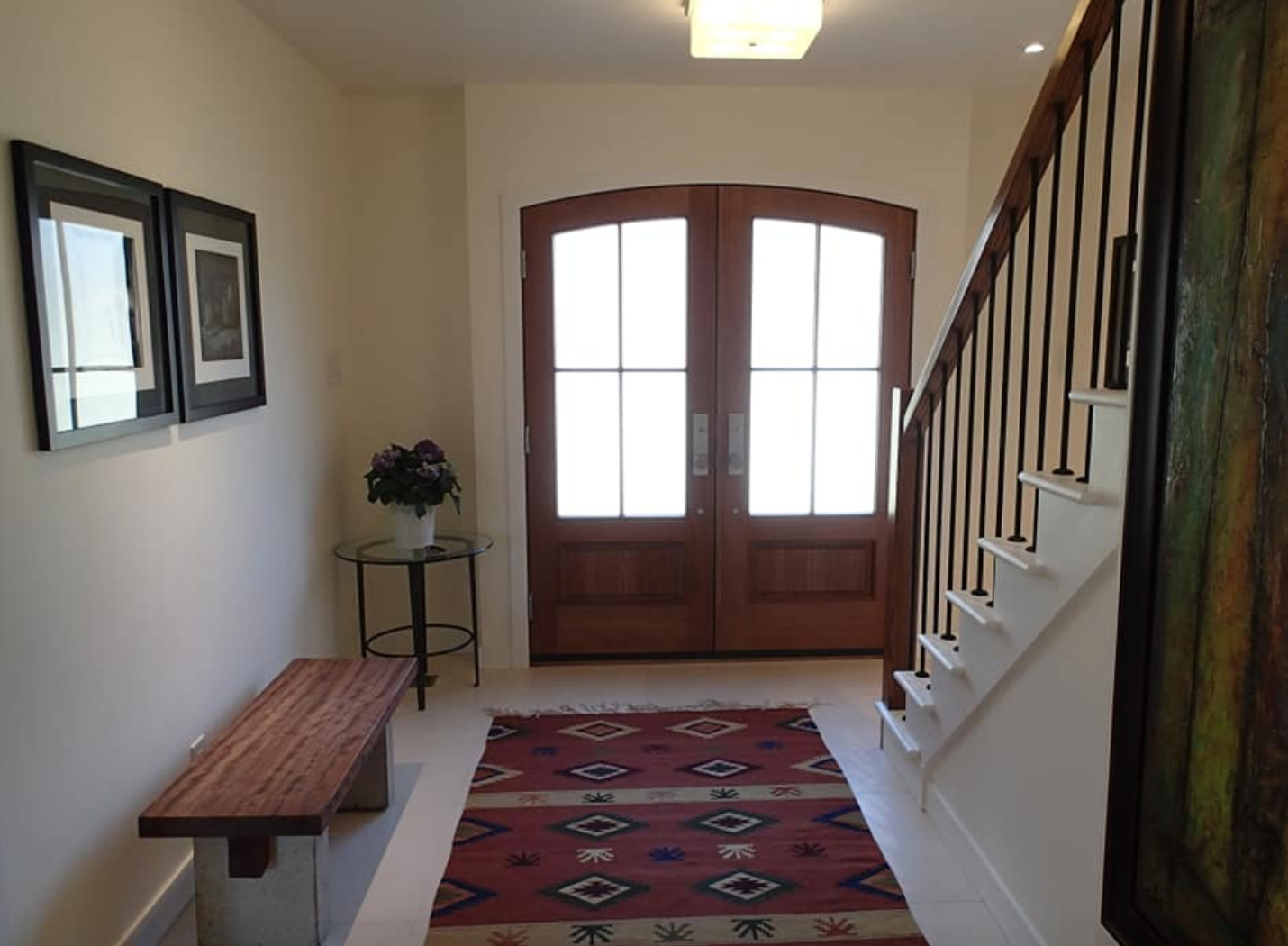 Entryway with wooden doors, staircase, rug, and artwork.