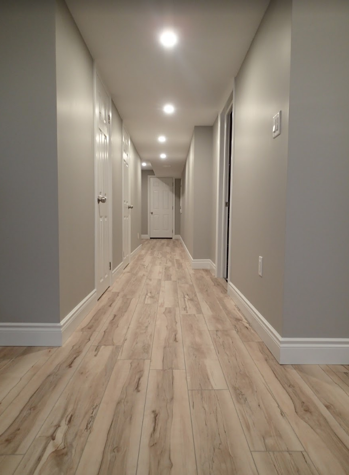 Long, empty hallway with light wood floors, gray walls, and white doors.
