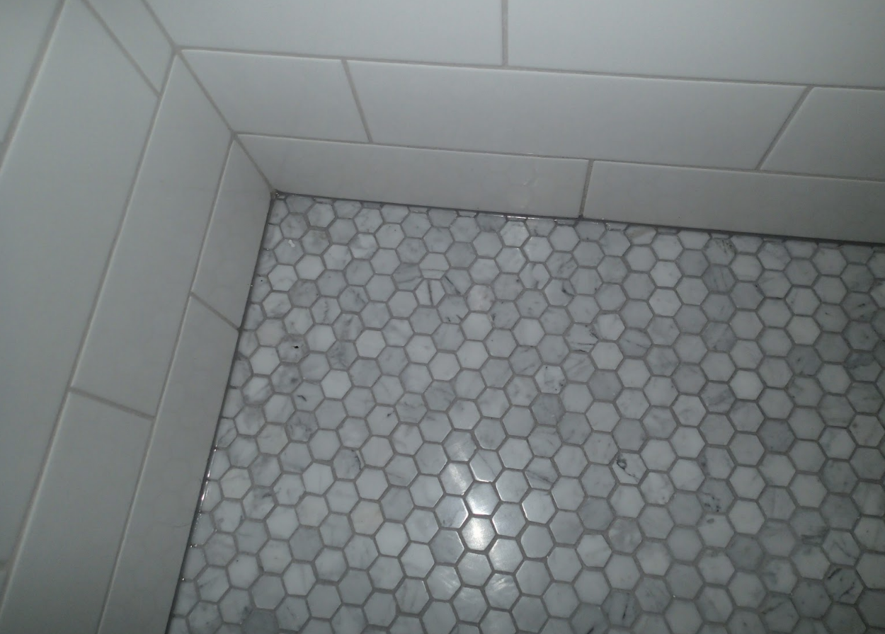 White and gray tiled shower corner. Hexagon mosaic floor, subway wall tiles.