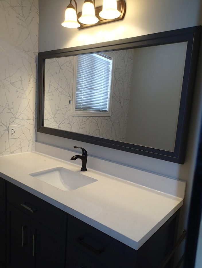 Bathroom vanity with a white countertop, dark cabinets, a black faucet, and a large mirror.