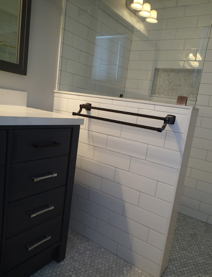 Bathroom interior with black vanity, white subway tile, glass shower, and a double towel bar.