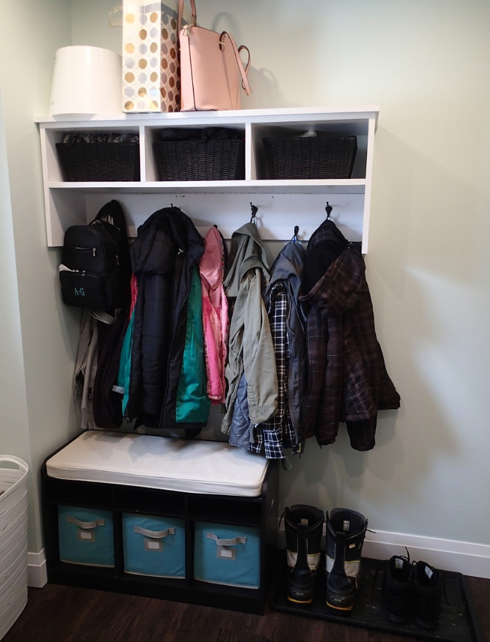Entryway bench with overhead storage, coats, and shoes. Black and white; blue bins; light green walls.