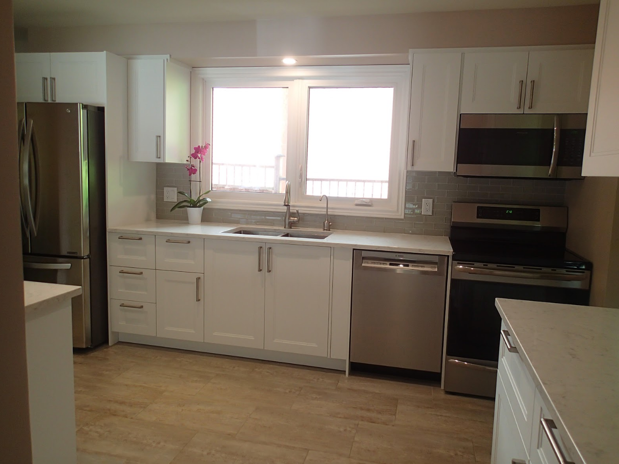 White kitchen with stainless steel appliances, white cabinets, and light-colored countertops.