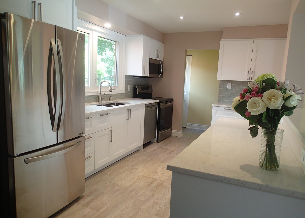 Bright white kitchen with stainless steel appliances, light countertops, and a bouquet of flowers.