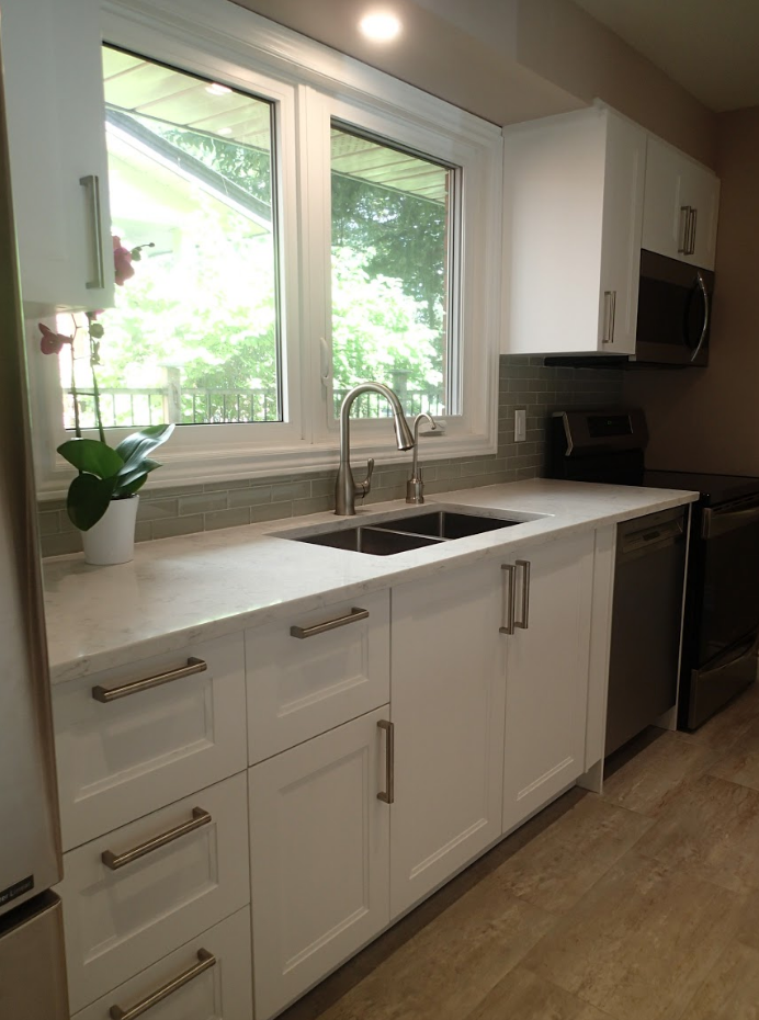 White kitchen with sink under window. White cabinets, stainless steel appliances.
