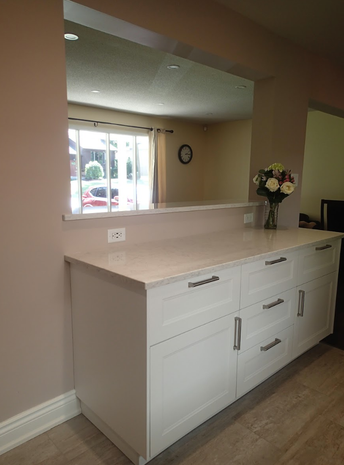 White cabinets with a light countertop and a pass-through to another room; a vase of flowers sits on the counter.