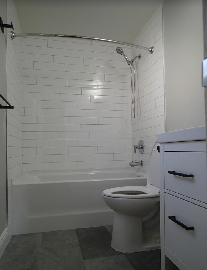 White-tiled bathroom with a tub, toilet, and vanity. The floors are gray.
