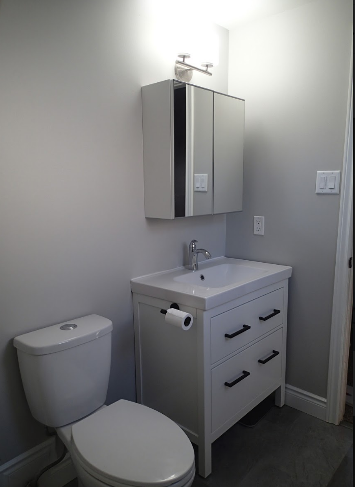 Small, gray-walled bathroom with white vanity, toilet, and mirrored medicine cabinet.