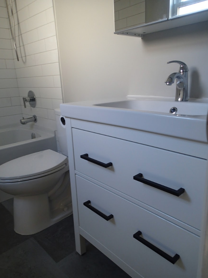 White bathroom with a sink, toilet, and tub. White cabinet with black handles. Chrome faucet.