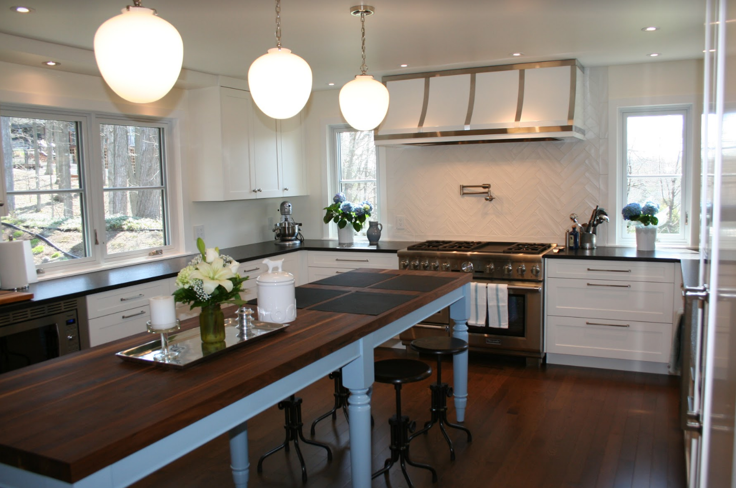 Bright white kitchen with dark wood island and stainless steel appliances; pendant lights hang above the island.