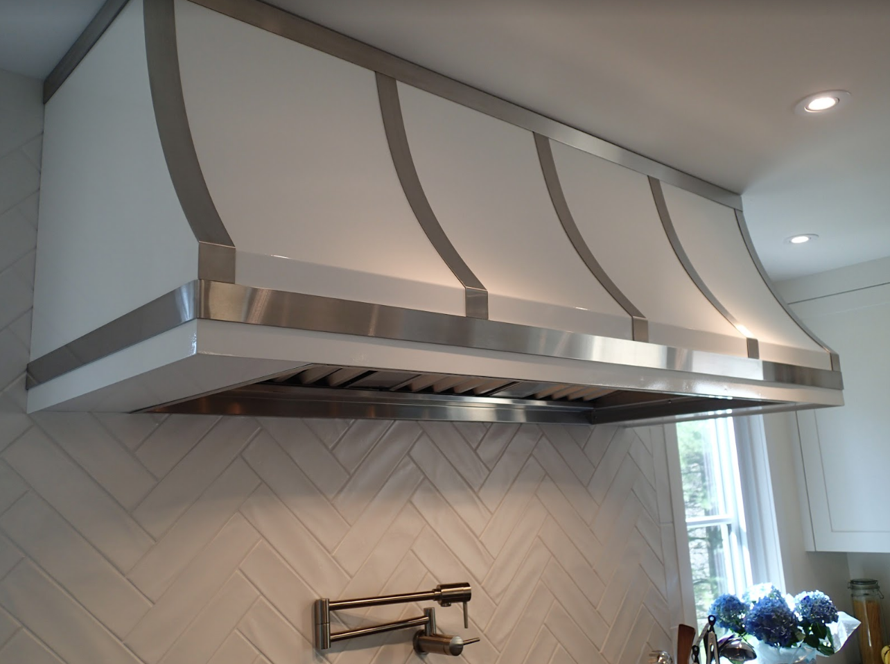 White and silver range hood over a herringbone tile backsplash.