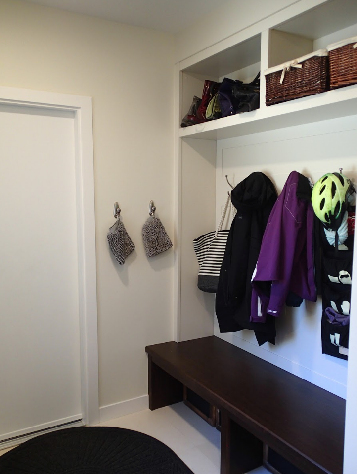 Mudroom with bench, coat hooks, storage baskets, and a door. White walls and dark wood accents.
