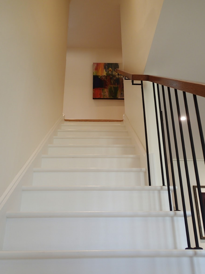 White stairs leading up, with a dark railing on the right, and artwork on the wall at the top.