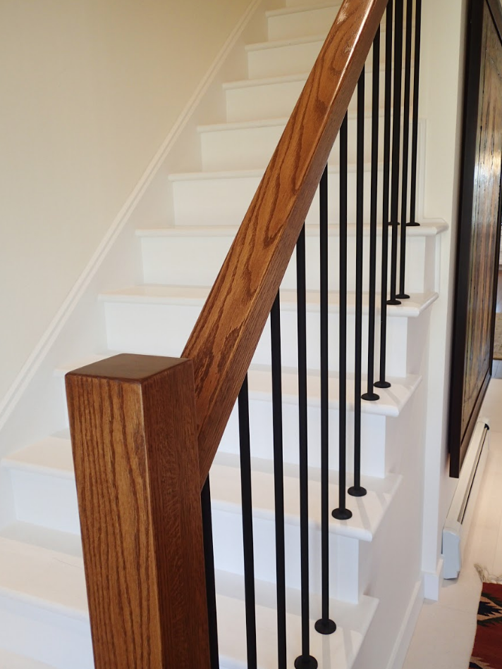 Staircase with white steps, wood handrail, black spindles, and a painting on the wall.