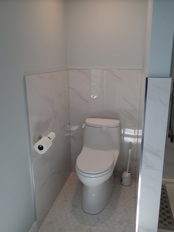 A toilet in a small bathroom with marble-like tiled walls and a gray floor.