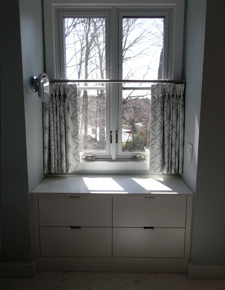 Window seat with white drawers, gray curtains, and a window overlooking trees.