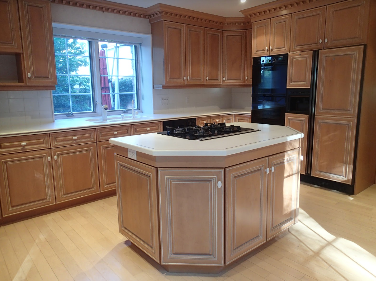 Kitchen with light brown cabinets, a white countertop island, and large window.