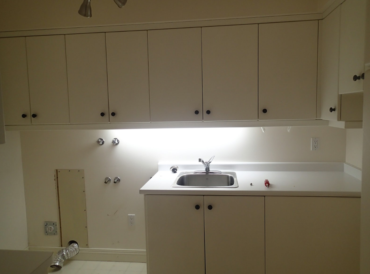 Laundry room with white cabinets, sink, and countertop. Upper cabinets span the wall, with a lower cabinet beneath the sink.