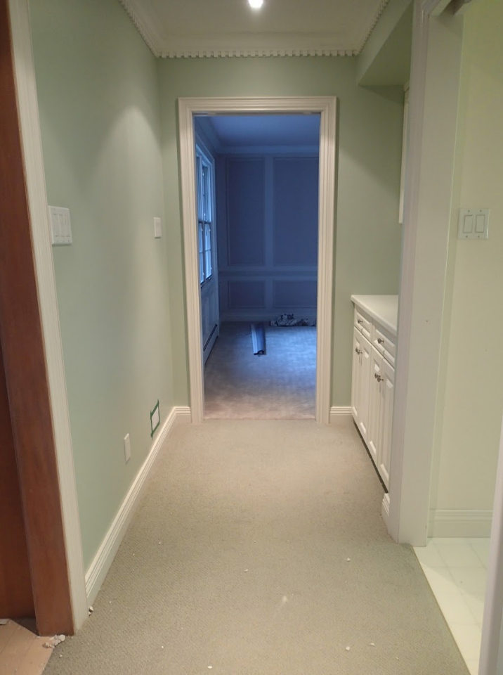 Hallway with light green walls, white trim, and a doorway leading to a room with a window.