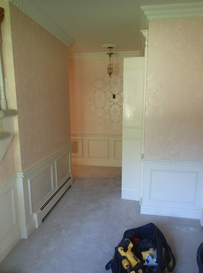 Hallway with pink patterned wallpaper, white trim, and carpet. A toolbox sits on the floor.