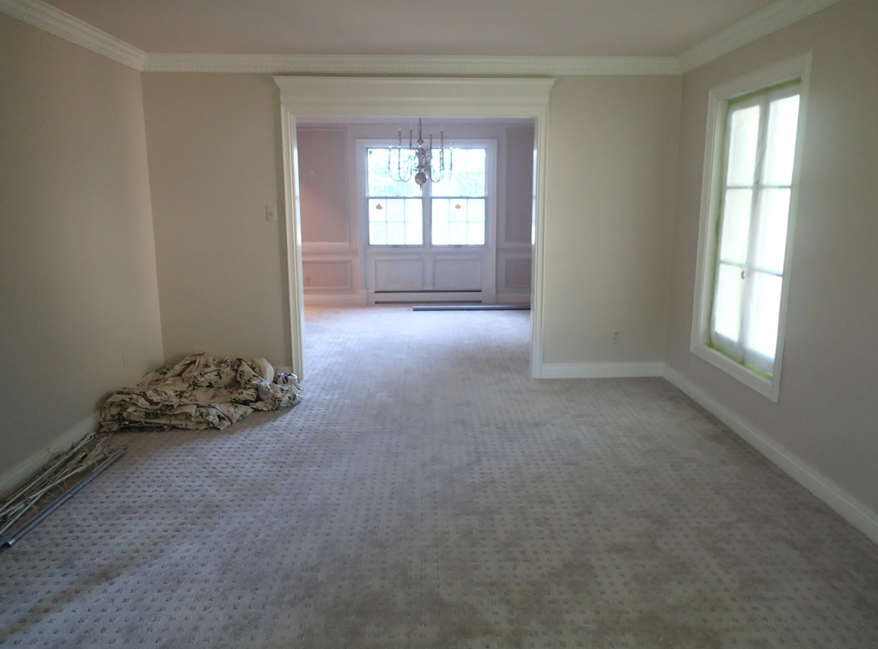 Empty room with beige walls, light carpet, and a doorway leading to a brighter space with a door.