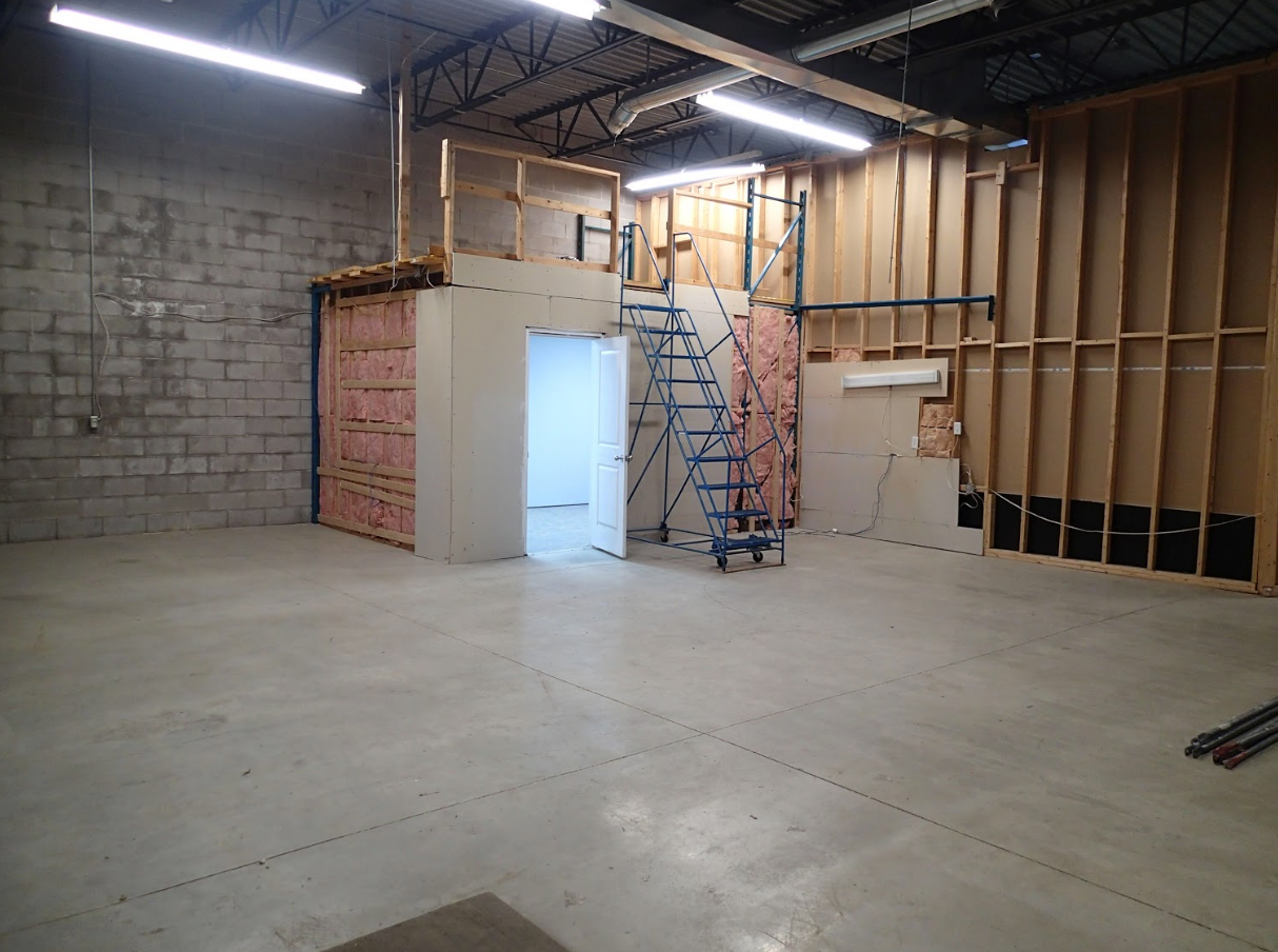 Empty warehouse with concrete floor, unfinished walls, and construction of a small elevated room.