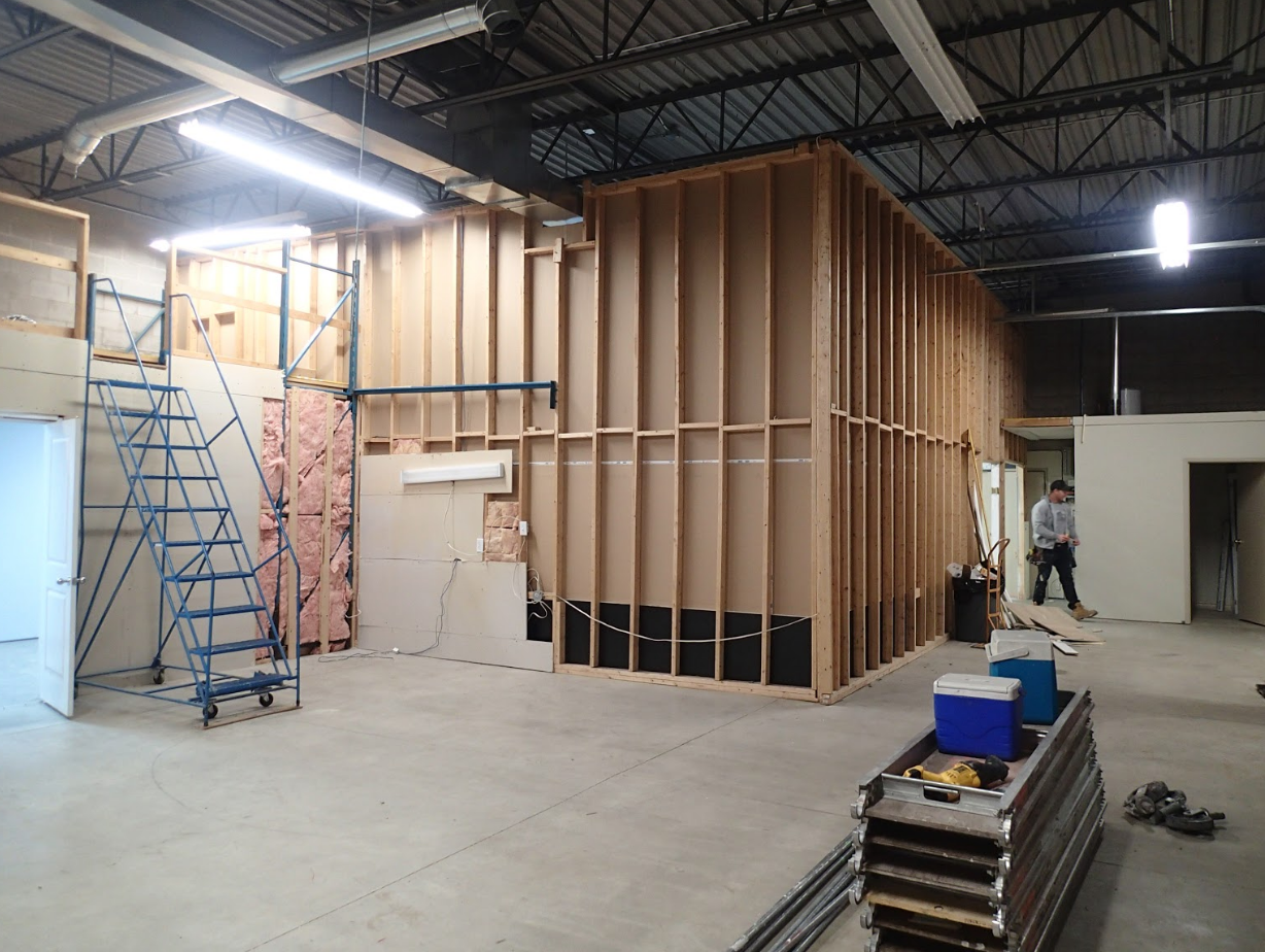 Interior under construction: wooden frames, unfinished walls, tools, person working, concrete floor.