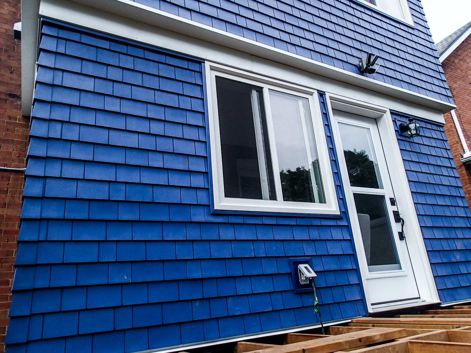 Blue shingle-sided house with white trim, window and door. Exterior view, daytime.