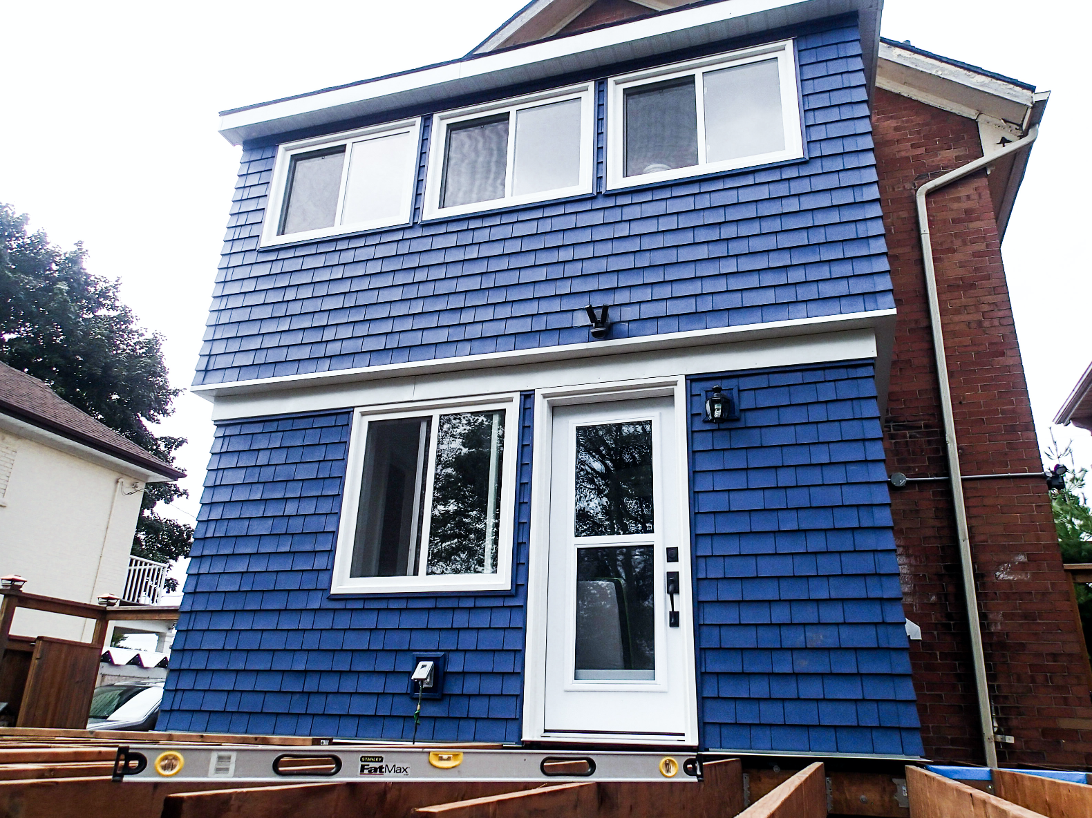Two-story blue shingled addition with white trim. Level in foreground, adjacent to brick house.