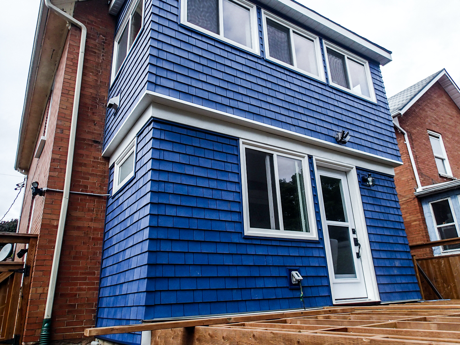 Blue-sided two-story addition to a brick building with white trim and a wooden deck.