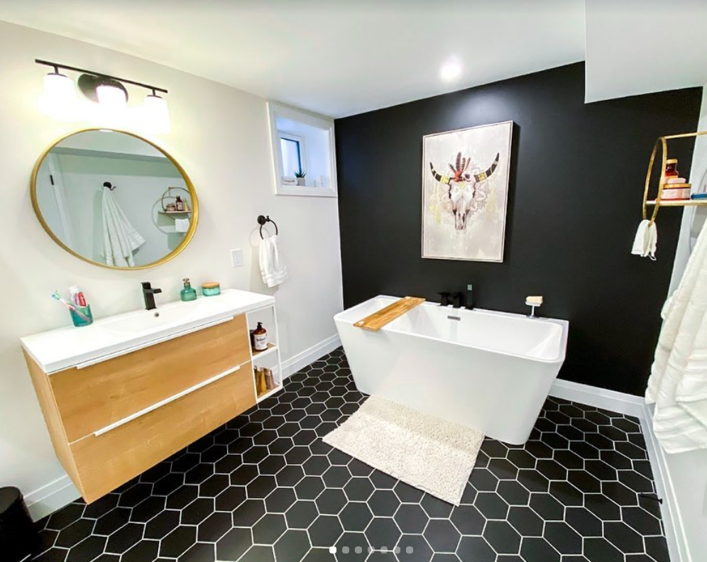 Modern bathroom with black hexagon tiles, white tub, and black accent wall with art.