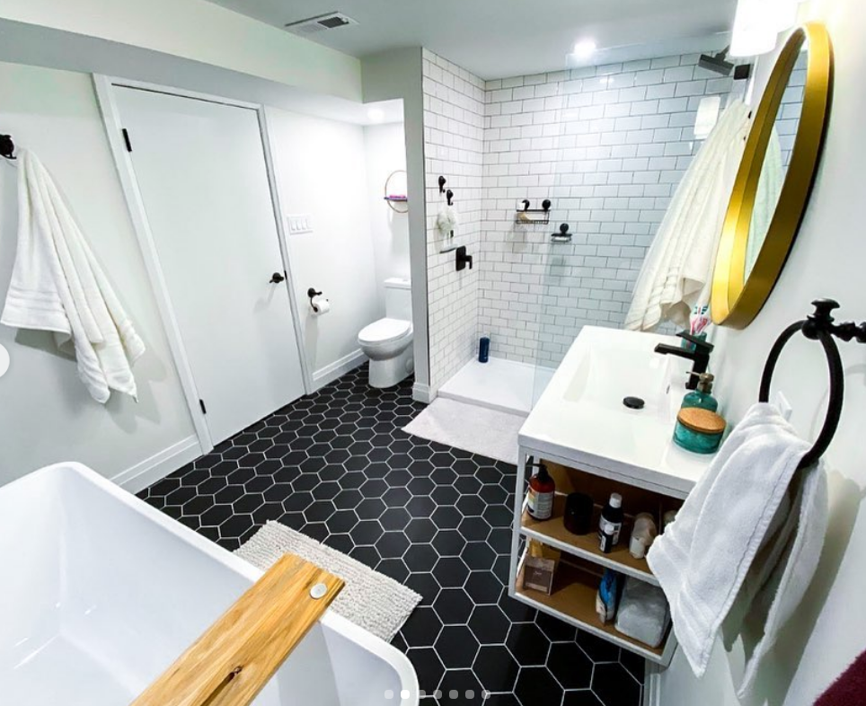 Modern bathroom with black hexagon floor, white subway tile shower, and gold mirror.