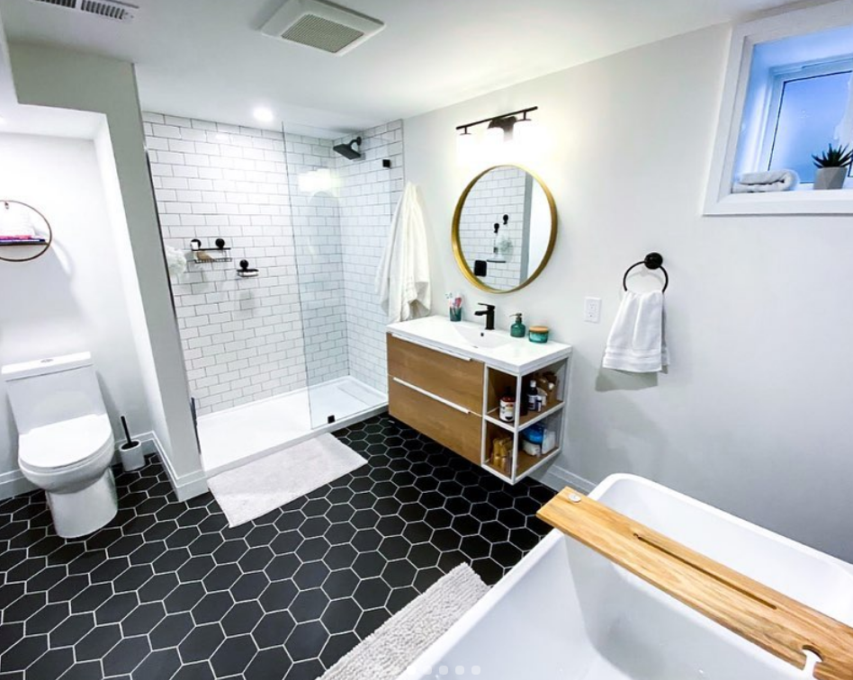 Bathroom with black hexagon floor tiles, white subway tile shower, floating wooden vanity, and a soaking tub.