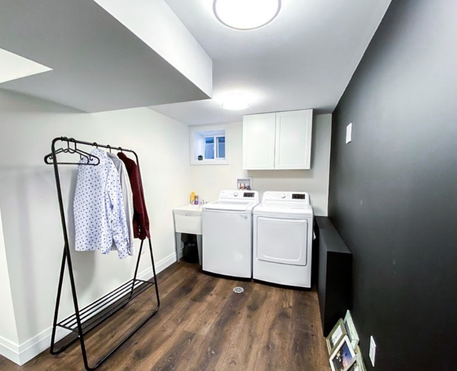 Laundry room with washer/dryer, hanging clothes, cabinets, and dark accent wall.