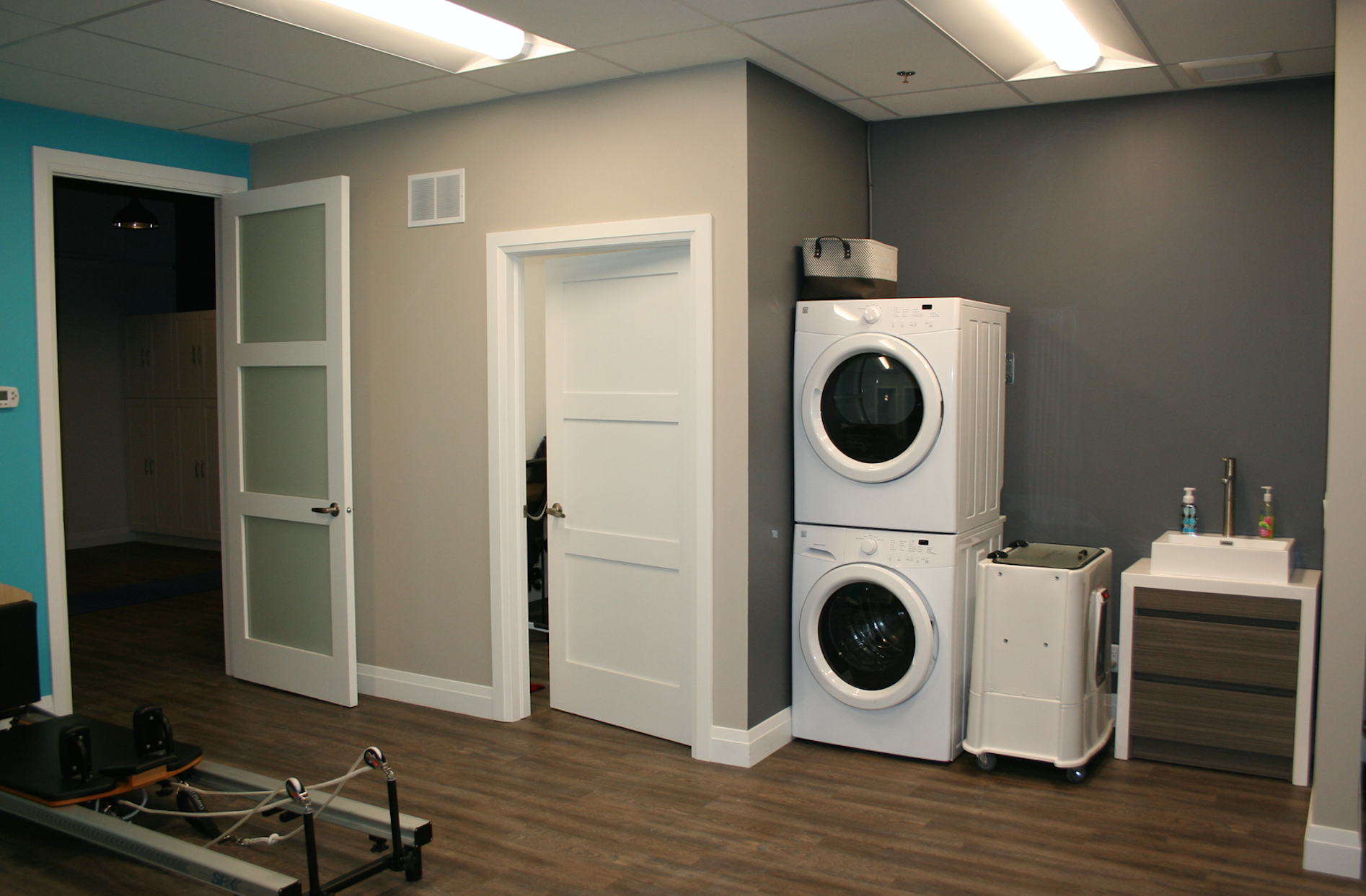 Laundry room with stacked washer/dryer, sink, and doors, gray, white, and teal walls.