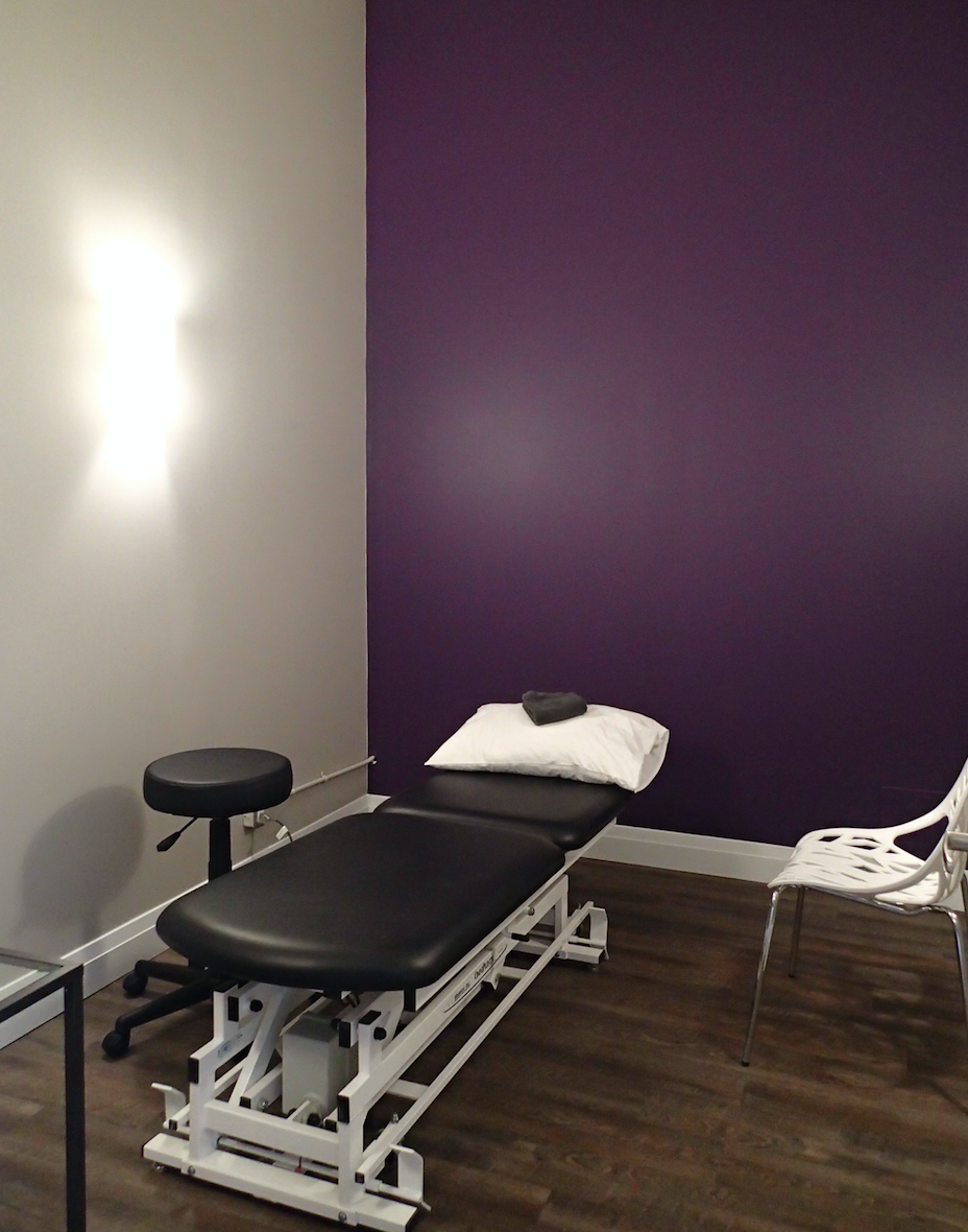 Examination room with purple wall, black massage table, and stool.