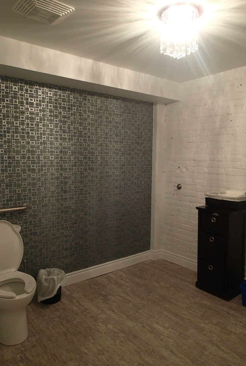 Bathroom with mosaic wall, toilet, small cabinet, and chandelier.