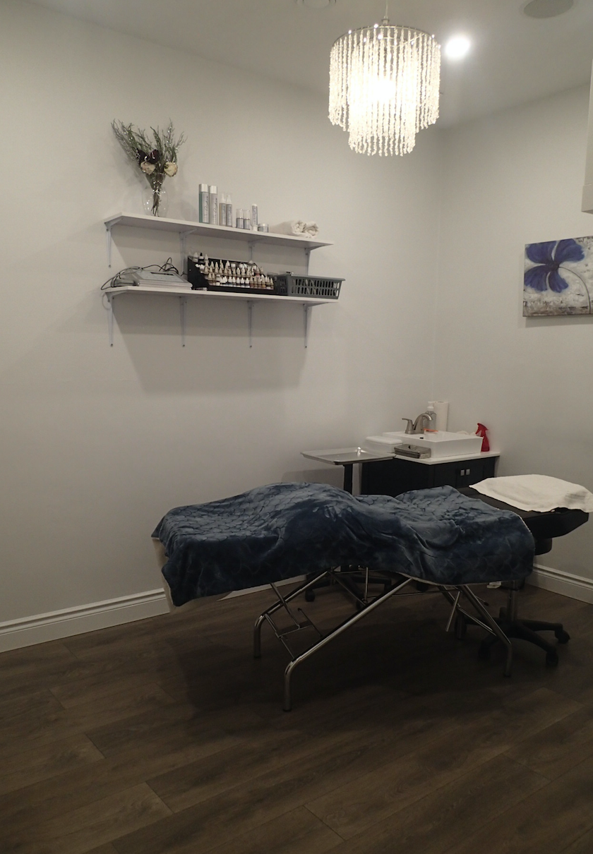 A spa room with a massage table, shelves of products, a decorative light, and a brown bag.