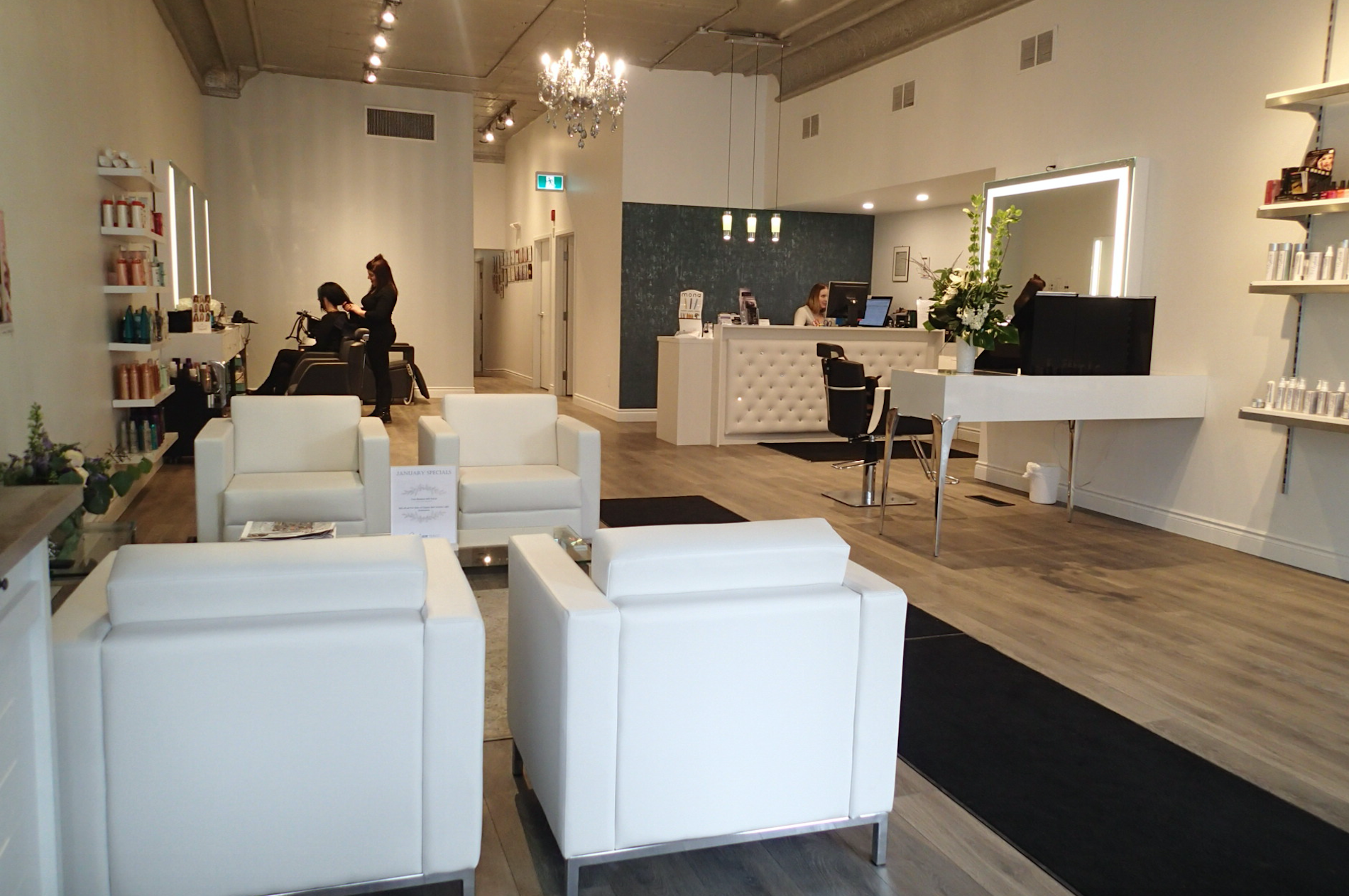 Interior of a hair salon with white chairs, a reception desk, and stylists working on clients.