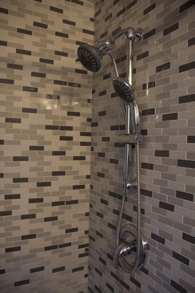 Shower with multi-head chrome fixture against a mosaic tile wall in shades of gray and black.