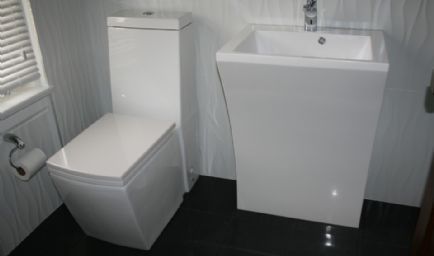 Modern white toilet and sink in a small bathroom with dark floor and textured walls.