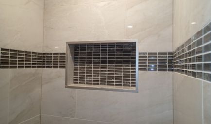 A tiled shower with a recessed shelf. Gray and black tiles with neutral gray walls.