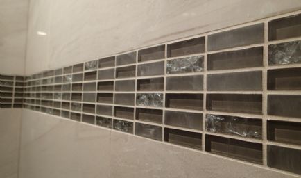 Horizontal row of rectangular gray and clear glass tiles set between white tiles on a wall.